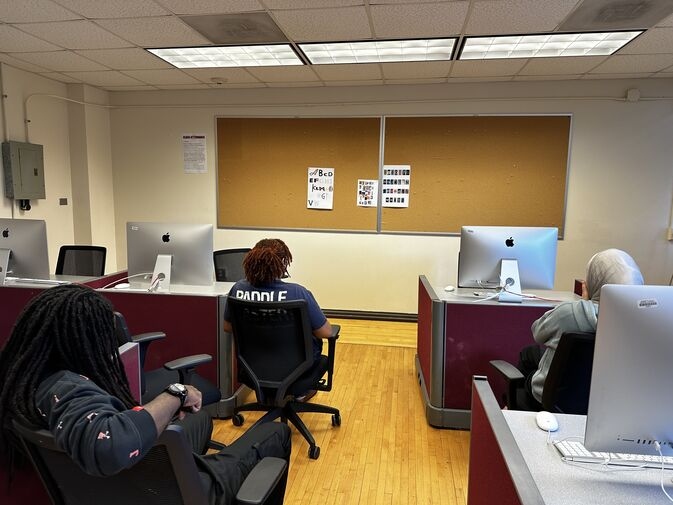 Several students sitting in a classroom looking at a cork board