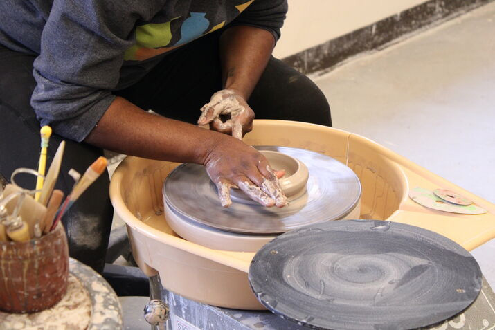 A student making a small bowl on a pottery wheel