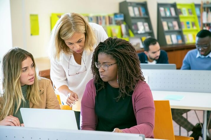 An instructor leaning down to talk to two sitting students