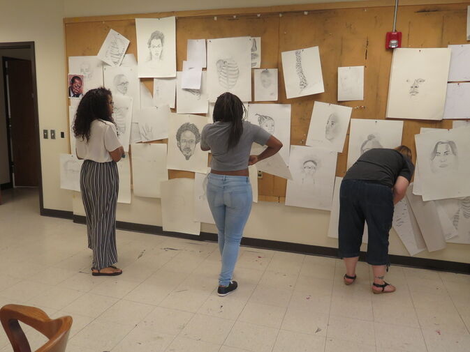 Three people looking at art pieces on a wall