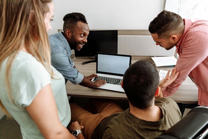 Several individuals looking at a laptop screen and talking