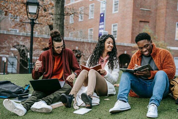 Three people sitting on a lawn and reading 