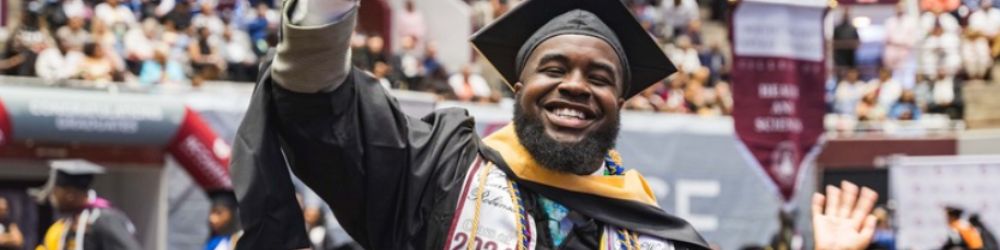 Male graduating student waiving his hand to the crowd during commencement.