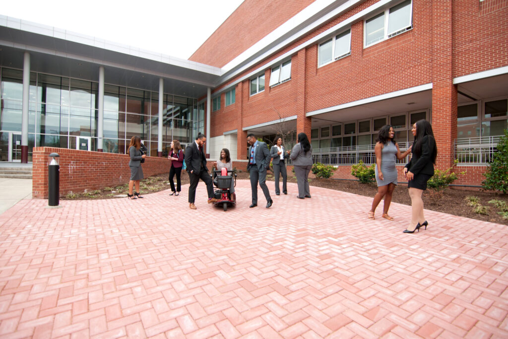 a group of people in business attire interacting with one another in front of the law school building. 