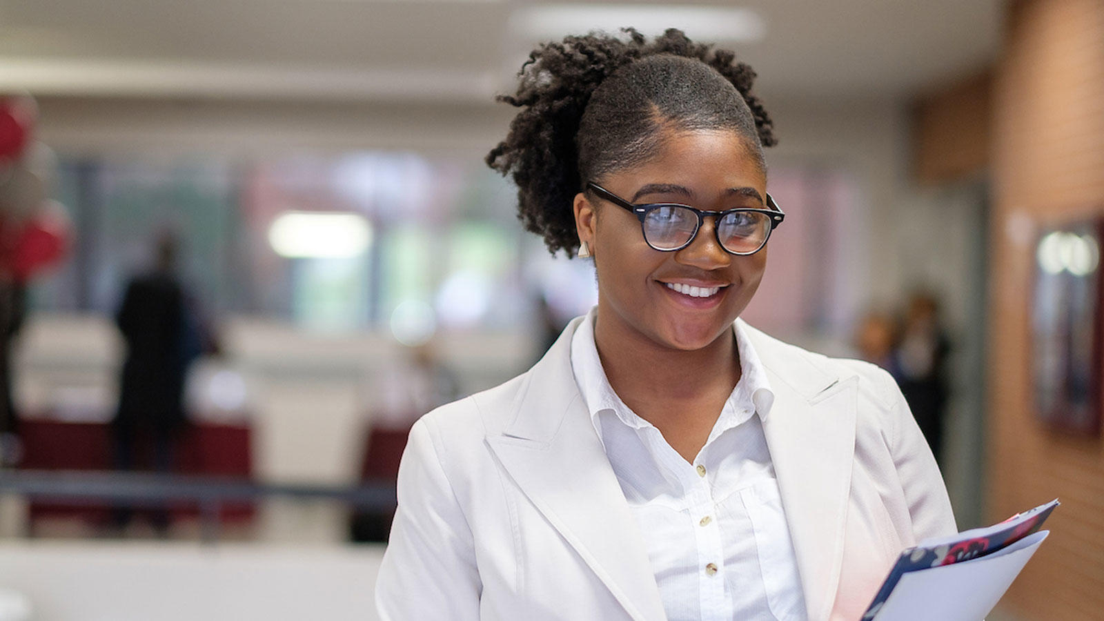 Student with glasses in all white attire, holding folders