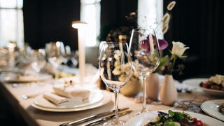 A place setting at a dining table with dishes, napkins, glasses and silverware.