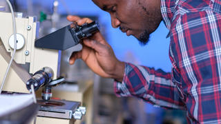 Man is looking into a microscope in a laboratory setting.