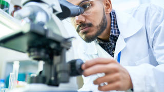 man in white coat looking into a microscope
