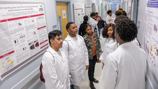 A dozen students stand in the hallway of a research laboratory.
