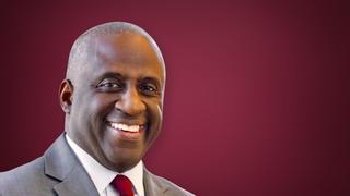 Man in suit smiling on a maroon background.