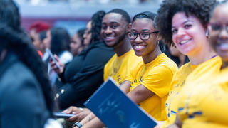Students in yellow shirts sitting at an event smiling towards the camera