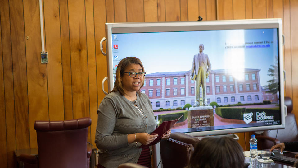 A woman in a suit giving a presentation in a boardroom 