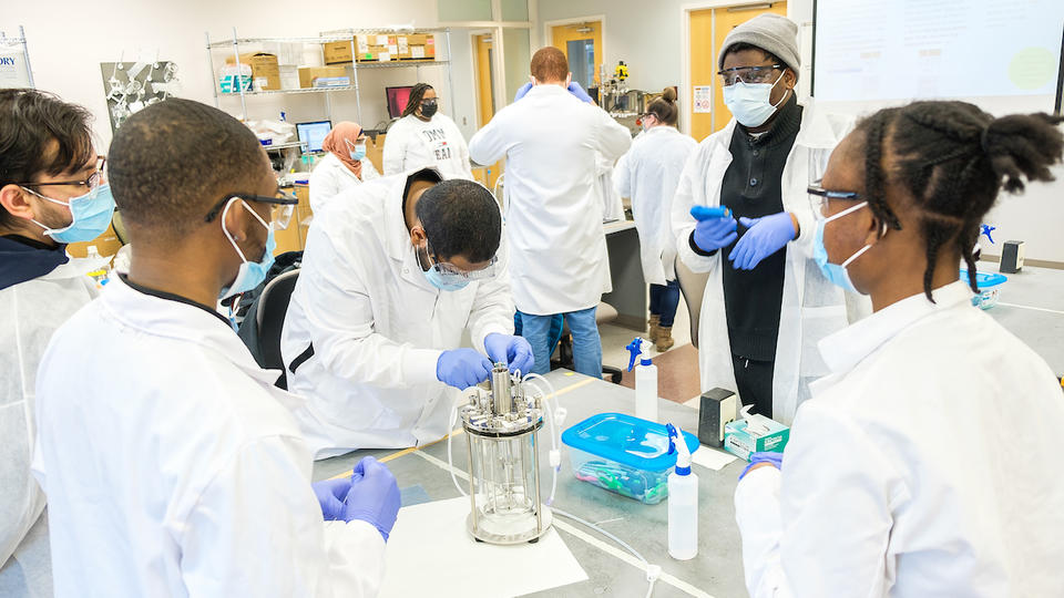 People in white lab coats gathered around a table discussing an experiment