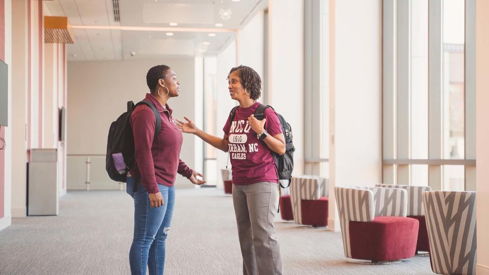 Two Office of E-Learning employees talking in the hallway