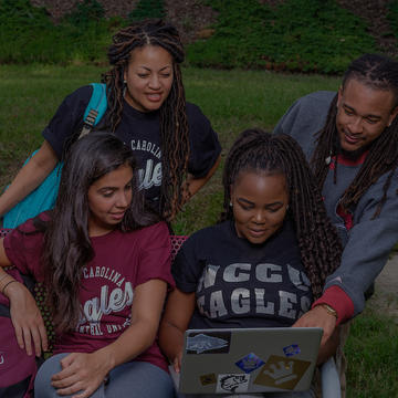 A Group of NCCU students looking at a laptop together while sitting outside